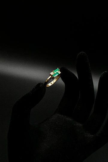 a person's hand holding a ring with a green stone
